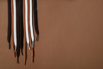 Different shoelaces on brown background, flat lay. Space for text