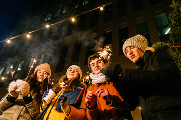 Group of happy four friends students have fun with sparklers at night party in the city. Love, relationship, season, friendship and people concept.