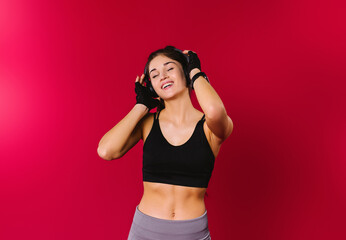 A cheerful girl with a beautiful physique with a smile listens to music in large headphones on a red background with empty side space.