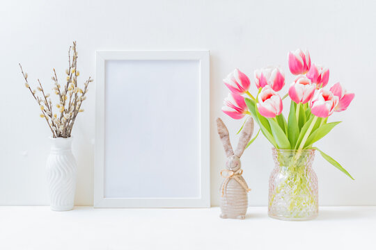 Home interior with easter decor. Mockup with a white frame and willow branches, pink tulips in a vase on a light background