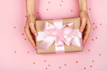 Beautiful female hand with minimalistic gift on a pink background with cute hearts. Concept of the Valentine's Day, surprises with love, holiday, etc.