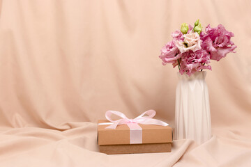 Bouquet of eustoma flowers and gift tied with ribbon on a beige cloth background. Romantic concept with copyspace. Present for 8 March or Mothers Day.