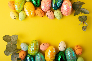 Fototapeta na wymiar Frame made from multicolored easter eggs.Fresh eucalyptus branch near it.Trendy yellow background.Creative layout with copy space.