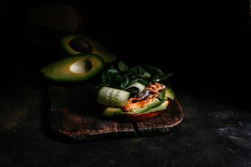sandwich with avocado red fish greens and cucumber on a dark background