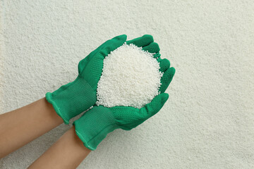 Woman holding pile of granular mineral fertilizer over grains, top view