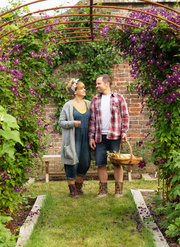 Couple harvesting vegetables below trellis with purple flowers