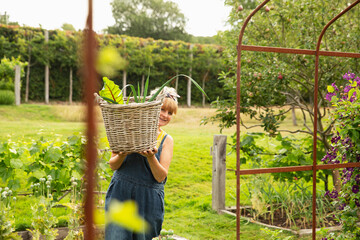 Portrait happy woman carrying basket of harvested vegetables in garden