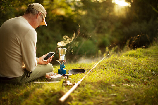 Man With Smart Phone Taking A Break From Fishing Making Coffee