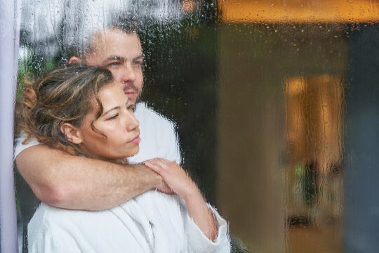 Serene affectionate couple hugging at rainy window