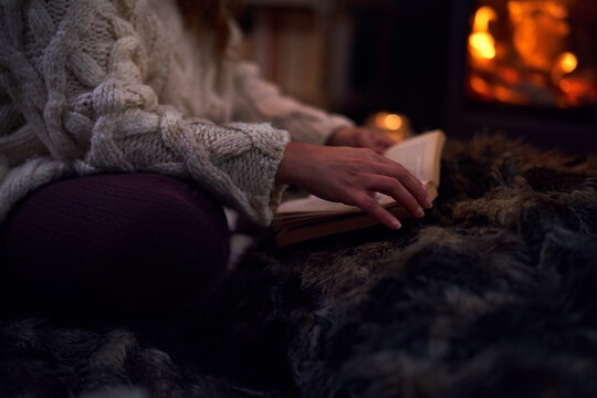 Woman reading book on blanket at cozy fireside