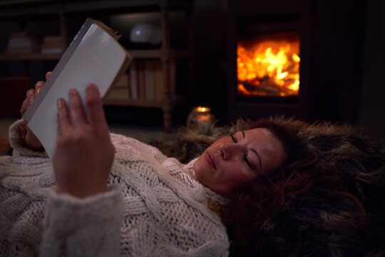 Woman relaxing reading book on blanket at cozy fireside