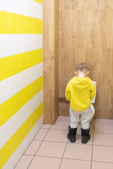 Child boy pissing in toilet bowl in children toilet with yellow tiles. Hygiene concept in public places.