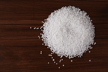 Pellets of ammonium nitrate on wooden table, flat lay with space for text. Mineral fertilizer