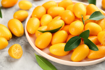 Fresh ripe kumquats in plate on light grey table, closeup