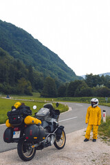 A girl in a yellow raincoat, shoe covers and a helmet. Motorcyclism and travel. Sightseeing tour. Mountains and hills. A gray day with thunderclouds. Difficult test and biker's outfit. Vertical photo