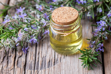 Rosemary oil. Rosemary essential oil jar glass bottle and branches of plant rosemary with flowers on rustic background.