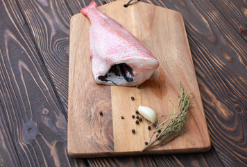 Fresh and ready to cook raw pink Perch fish with ingredients like lemon and carrot on a wooden pad,...