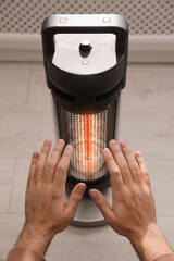 Man warming hands near modern heater indoors, closeup