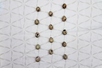 A lot of quail eggs on a white tablecloth with square designs. Small quail eggs in line
