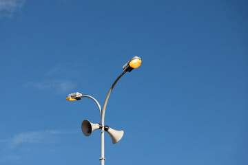 Street lights turned on during a sunny day. Electricity waste, consumption society. City lights with blue sky