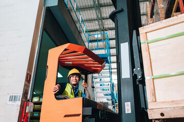 Fototapeta premium Worker driver asian man in protective safety jumpsuit uniform with yellow hardhat at warehouse forklift loader works