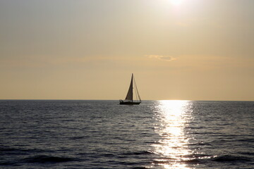 Fototapeta na wymiar Sailboat on the horizon backlit with the ray of sun setting over the sea