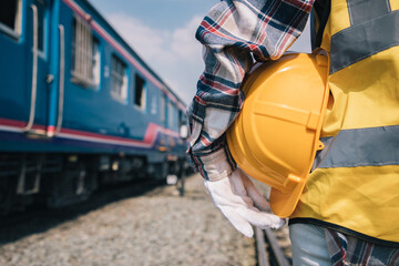 Back view of train engineering standing and holding hardhat at work outside. Background of modern train with railway for transportation. Service and technician concept.
