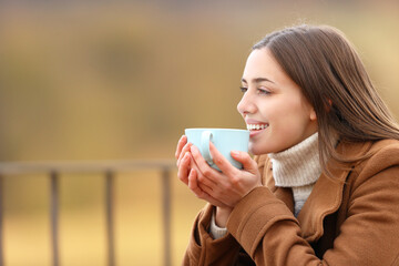 Happy woman drinking coffee in a terrace in winter