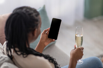 Unrecognizable black woman with glass of champagne using smartphone