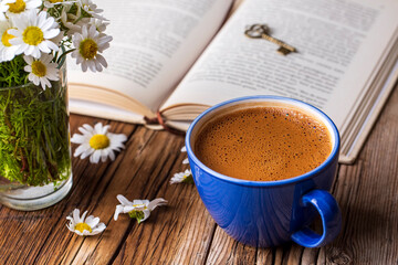 A cup of coffee with a book and daisies