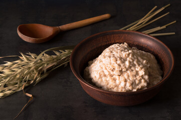 Oatmeal porridge in a vintage clay bowl with ears of oats on a dark table background.