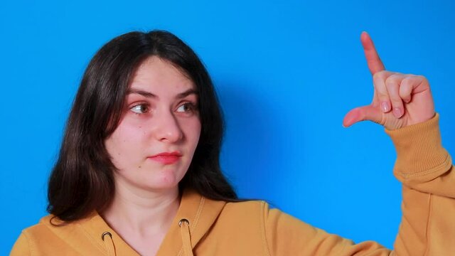 A brunette woman on a blue background shows a finger of rising earnings, a level of success in business and achievement, an increase in income.