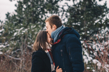 Portrait of a couple, man kissing woman on forehead, on a winter outdoor background