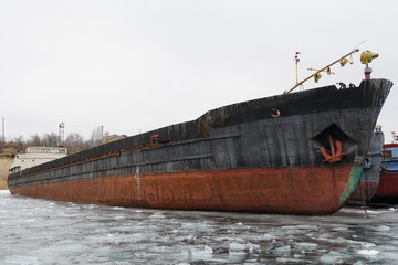 Fototapeta premium Old rusty motor ship. Wintering ships on a frozen river in their port. Volgograd. Russia