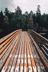 embrace the unknown text quote on wooden bridge towards the woods