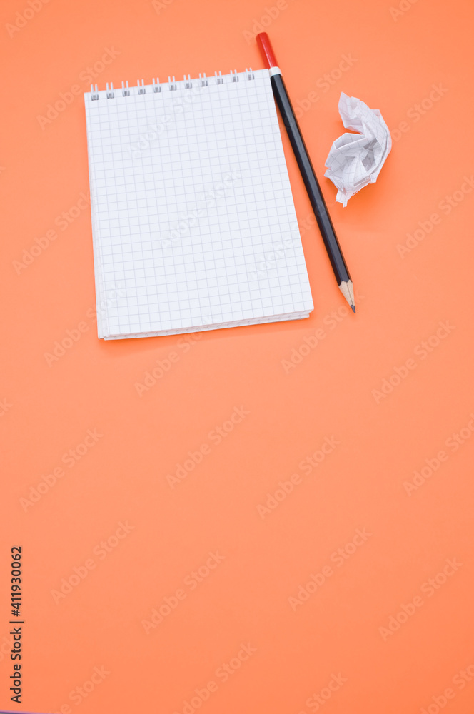 Poster overhead shot of a pencil on a grid notepad and a crumpled paper isolated on an orange background