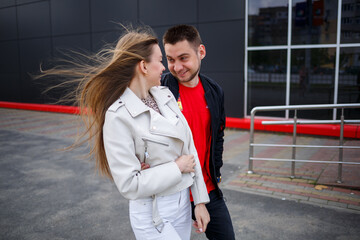 Stylish young girl with blond hair of European appearance and a guy in a black jacket. Urban walk of a couple in love, modern fashion in casual style. Happy relationship concept