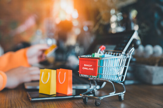 Online shop concept, ecommerce marketplace, payment, Selective focus cart and shopping bag with blurred woman hands making payment with credit card on laptop