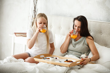 Having family breakfast in bed concept. Young happy mother eating pancakes and drinking orange...