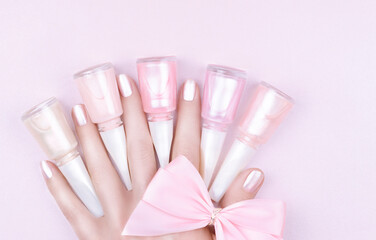 Female fingers with pastel pink manicure and nail polishes on a pink background.