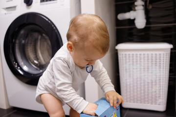Infant boy open box with tablet for dishwasher or detergent in bathroom alone