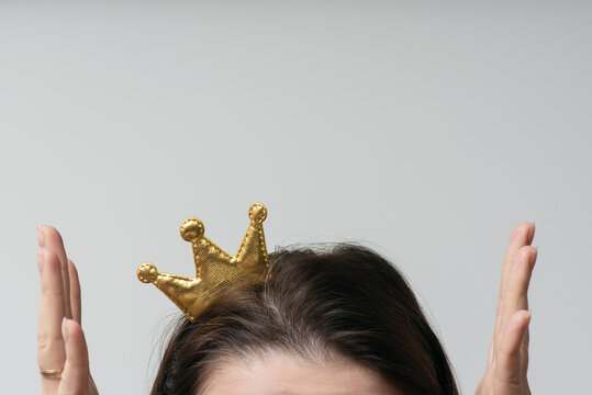 Surprised girl with a golden crown on her head is raising up her hands close up. Vip.