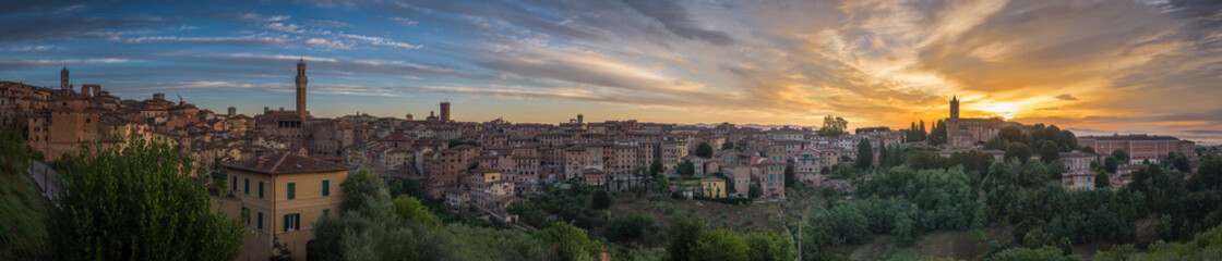 Panorama of Siena old town at sunrise, a medieval and Renaissance city in Tuscany, Italy, with Mangia tower, church, old houses and palaces on a green hill