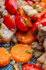 Baked carrot pieces, cherry tomatoes, garlic with small pieces of meat. Green onions. Shallow depth of field.