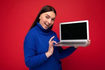 Naklejka premium Photo of beautiful young woman holding computer laptop looking at camera isolated over colourful background
