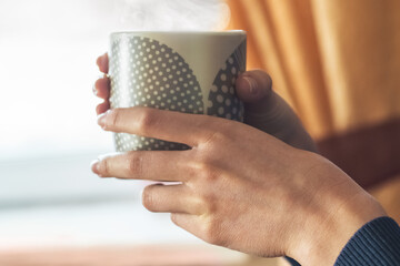 Cup with hot coffee in the hands of a young girl, morning coffee