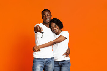 Happy black couple with new car keys smiling on orange
