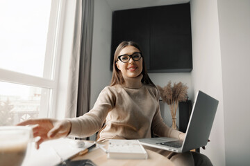 Beautiful happy woman working at home with laptop taking cup of coffee . Smiling business woman woman wearing eyeglasses in office,  using laptop computer