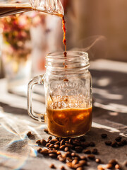 Close-up of a cup of coffee, hot coffee is poured from a jug in a stream into a cute cup on a sunny background with flowers. The concept of restaurants and coffee shops