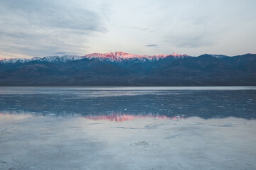 Alpenglow on Telescope Peak at sunrise. Mountain reflections on wet salt field of Badwater in Death Valley.